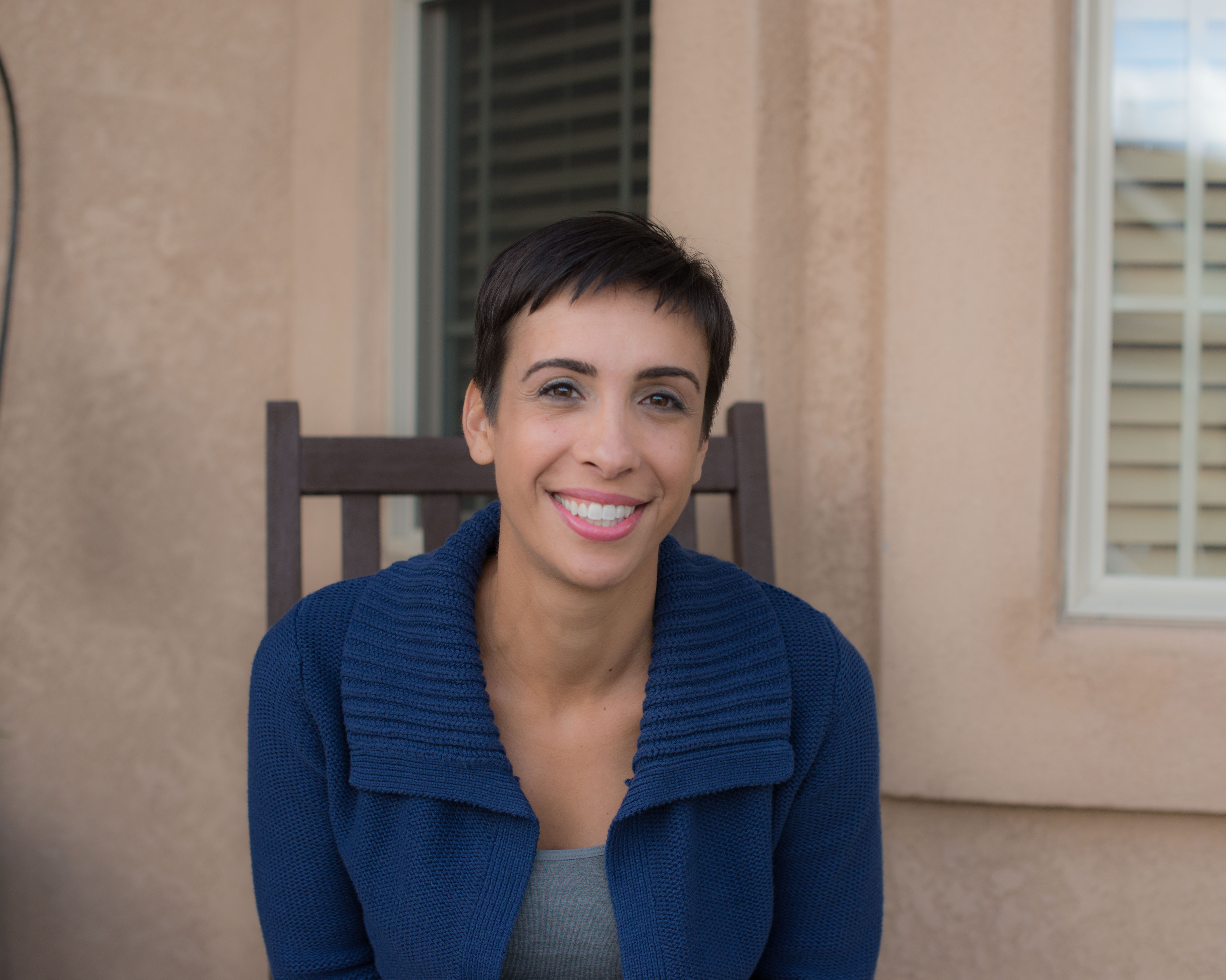 Portrait of Dani, survivor of sexual abuse, seated in a chair against a tan background with windows